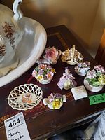 Photo showing the full lot of Royal Adderly china floral miniatures and figurine, arranged on a wooden surface with a vintage wash basin partially visible.