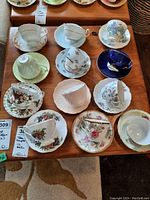 Overview of all 12 teacups and saucers with various floral patterns arranged on wooden table