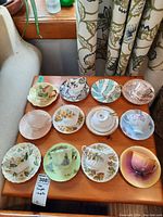 12 sets of assorted china teacups and saucers laid out on wooden table