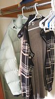 Light green puffy jacket and sleeveless plaid vest hanging on hangers in a closet