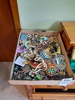Cardboard box filled with assorted costume jewelry: necklaces, bracelets, brooches, earrings