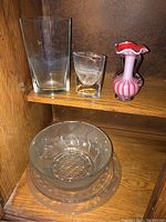 Shelf showing four glass vases (one pink ruffled edge, three clear) on top and clear glass bowl and platter below.