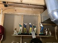 Seven golf figurines displayed on a basement shelf, various swing poses, assorted clothing colors, some with golf clubs and one with golf bag.