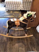 Full view of the rocking horse showing the dark brown plush body, wooden rockers, tan saddle, and yarn mane and tail.