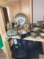 Photo of metalware lot showing horse figurines, decorative horse plates, varying metal bowls and candleholders on wooden shelf.