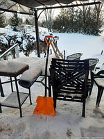 Metal outdoor furniture set consisting of rectangular table and four stacked metal chairs, covered in snow under a canopy.