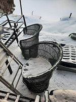 Two round rattan chairs outdoors on snow-covered patio showing weathering and slight damage to paint and rattan weave.