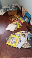 Several vinyl record albums laid out on a hardwood floor in two piles showing a variety of album cover art.