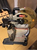 Front angled view of Ryobi miter saw showing the blade, safety guard, handles, and angle adjustment base.
