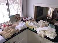 Wide view of assorted table linens laid out on a black countertop, including lace tablecloths, white fabric cloths, and colorful printed items.