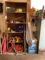 Wide angle showing shelving unit with ratchet straps, pipe clamp, propane torch, rolls of screening, and other garage items.