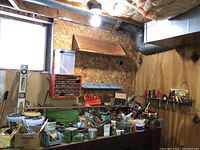 Wide view of basement workbench area with various hand tools, containers, and metal parts scattered and organized in drawers and boxes.