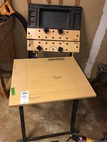 Two Craftsman folding work tables in basement with wooden tops and metal legs; one table has a pegboard style top and the other a smooth wooden top with Craftsman branding and measurement markings.