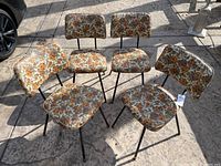 Four vintage kitchen chairs arranged in a semi-circle outdoors on a stone surface, showing the full set and style