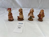 Four wood carved figurines displayed side by side on white fabric background. Includes a card with lot number 39.