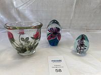 Wide view of the three art glass pieces: orchid paperweight, swirl paperweight, and rose bowl