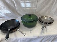 Full lot showing four cookware items including a green Dutch oven, one black non-stick frying pan, and two stainless steel frying pans.