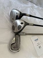 Three golf clubs laid on a surface showing the club heads clearly: Titleist 975D driver, Titan fairway wood 7, and Jack Nicklaus Custom Performance iron.