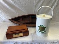 Photo showing wooden canoe model, wooden tissue box with plaque, and white ceramic ice bucket with gold handle and 1975 Cracker Invitational logo.