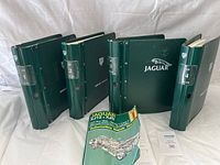 Four green binder-style Jaguar XJS service manuals arranged in a row with a Jaguar XJ12 & XJS automotive repair manual booklet in front.