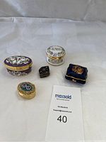 Overview photo showing all six small pill or trinket boxes of various designs and origins on a plain white fabric background.