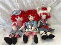 Photo showing three vintage Raggedy Ann dolls seated on white fabric background