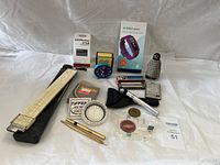 Photo showing entire assortment of items including slide rule, remote, Fitbit box, clock, pens, harmonica, ashtray, tool, and brochures.