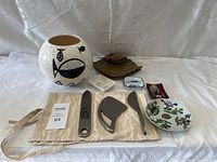 Wide shot of all items showing ceramic vase with fish design, kitchen utensils in fabric pouch, small decorative plates, and vintage Capri item.