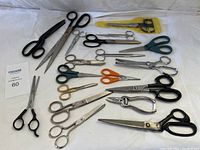 Full view of all 18 scissors and cutting tools arranged on white surface showing variety of sizes and styles.