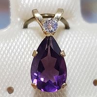 Front view of the 10K yellow gold pendant showing the pear-shaped purple amethyst and the smaller round clear stone.