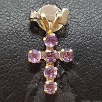 Close-up front view of the cross pendant showing six round amethyst stones set in yellow gold prong settings and the attached gold bail.