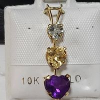 Front view of the pendant showing the three heart-shaped gemstones (clear, yellow, and purple) set in 10K yellow gold.