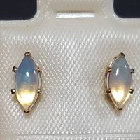 Front view of both marquise-shaped opal earrings in yellow gold setting placed on white textured background.