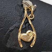 Close-up of a 10K yellow gold pendant in wishbone and heart shape, shown on black textured background.