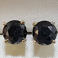 Front view of pair of stud earrings with round black diamonds set in yellow gold four-prong settings