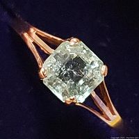 Close-up photo showing the emerald cut stone with prong setting on a 14K gold band, showcasing the stone's rectangular shape and inclusions.