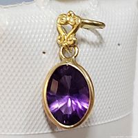 Close-up image showing the oval faceted purple amethyst gemstone bezel set in 14K yellow gold with decorative bail design.
