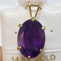 Close-up front view of oval faceted deep purple amethyst gemstone set in 14K yellow gold pendant with six prongs and wide bale.