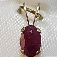Close-up front view of 14K yellow gold pendant with an oval ruby gemstone set in four prongs.