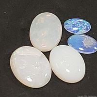Five polished oval opal stones on dark fabric background showing different body tones and color play.