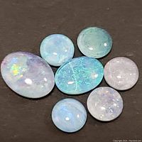 Seven genuine opal triplet cabochon gemstones arranged on black background showing color play and various sizes.