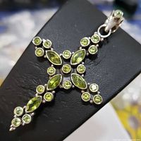 Close-up image showing the front view of the sterling silver cross pendant with multiple apricot-green peridot stones set in round and marquise shapes.