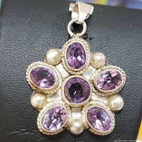 Close-up front photo of the flower-shaped sterling silver pendant with six oval amethyst stones and silver balls on black surface