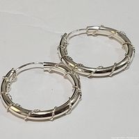 Pair of sterling silver hoop earrings shown individually and overlapping on white background, highlighting twisted wire detail and latch clasps.