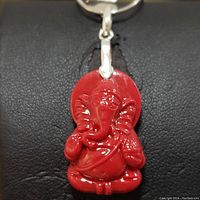 Close-up front view of red Ganesha pendant necklace on black background showing detailed carving and shiny silver bail.