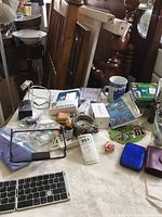 Overview of assorted household and personal items on a table including light switch, mugs, keys, cables, and stationery.