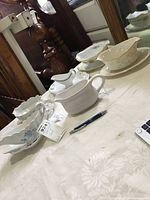 Overview of multiple porcelain gravy boats and underplates arranged on a table with a pen for scale.