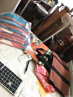 Photo shows four bags including a brown rolling expandable luggage bag, a turquiose and orange fringe bag by Thirty-One with a llama design, a small pink patterned bag, and a plastic paisley bag sealed in plastic.