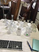 Wide view of multiple clear glass candlesticks in various shapes and sizes arranged on a table.