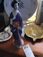Front view of the porcelain Geisha bottle figurine in purple kimono, displayed with other decorative items.